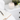 Open journal with handwritten notes and pen on a white bed beside a lit candle and fresh white flowers on a nightstand — a calming space for mindful journaling.