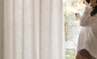 Woman enjoying a slow morning with coffee by the window, embodying soft life living with calm, cozy routines and natural light.
